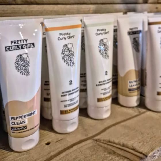 Tubes van Pretty Curly Girl op een houten plank in de salon: shampoo, conditioners en leave-in.