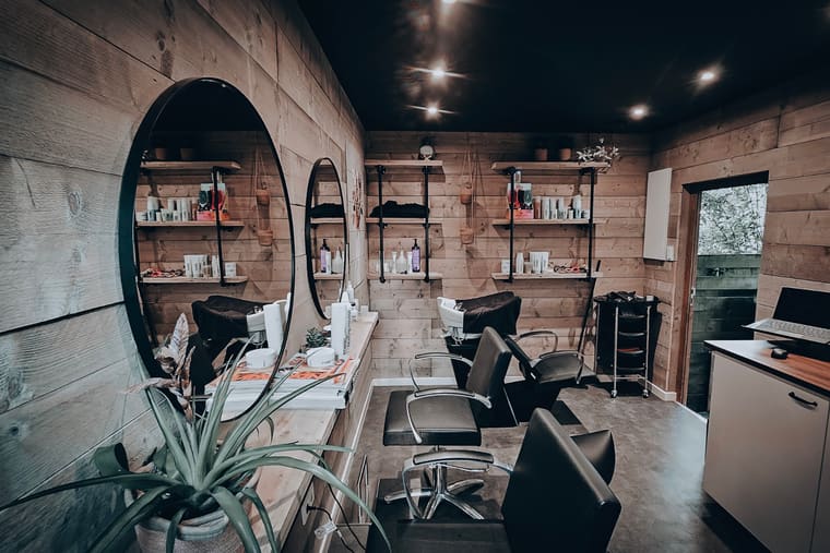 De salon van Haar&Zo in Soest: houten wanden, ronde spiegels, kappersstoelen en planken met haarproducten.