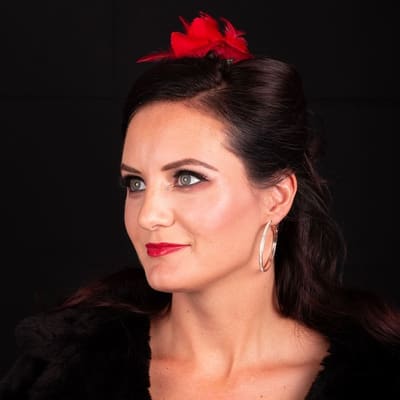 Make-up met donkere ogen en rode lippen, van opzij gezien; rode veer in het haar.